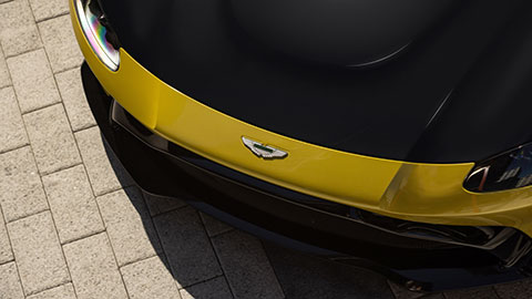 A close‑up view of a sports car hood featuring a yellow center section bordered by black paint, with the vehicle emblem visible near the front.