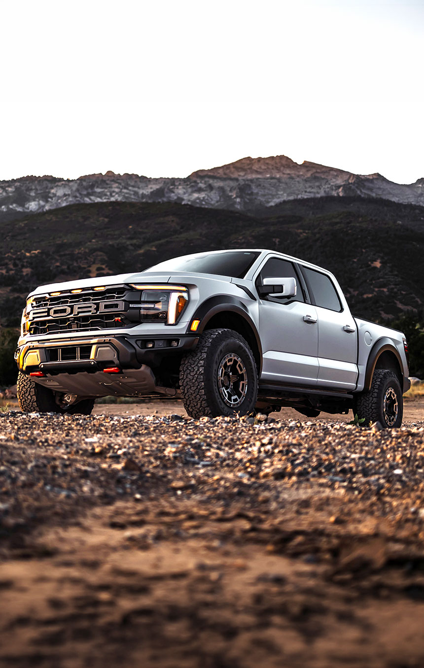 Silver off‑road pickup truck parked on rocky terrain with mountains in the background, showcasing rugged performance and durable exterior features. 