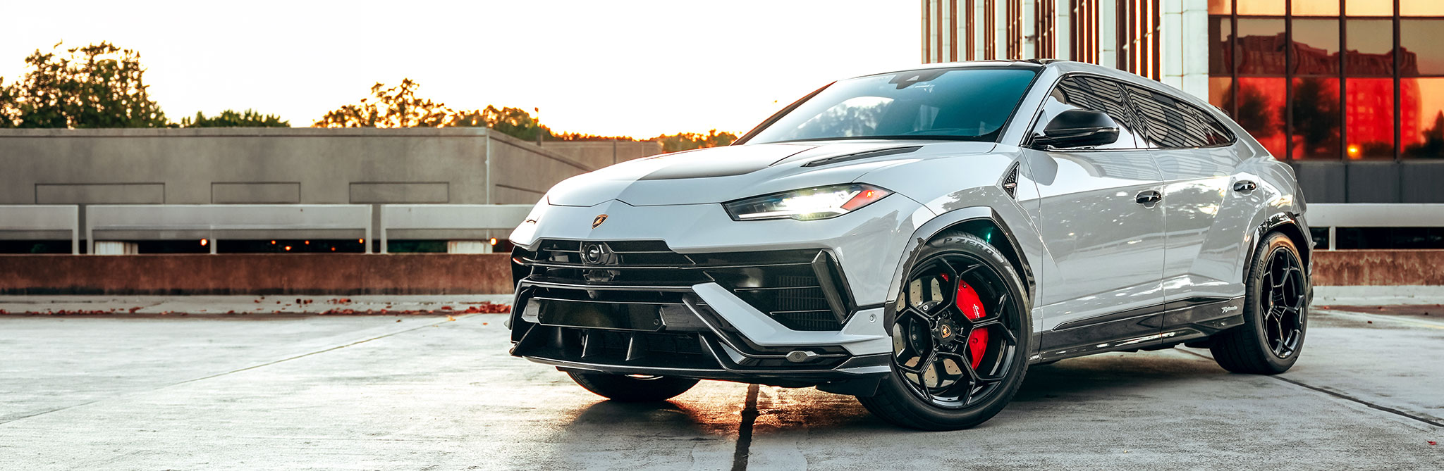 A silver performance SUV parked on a rooftop at sunset, shown from a front three‑quarter angle. 