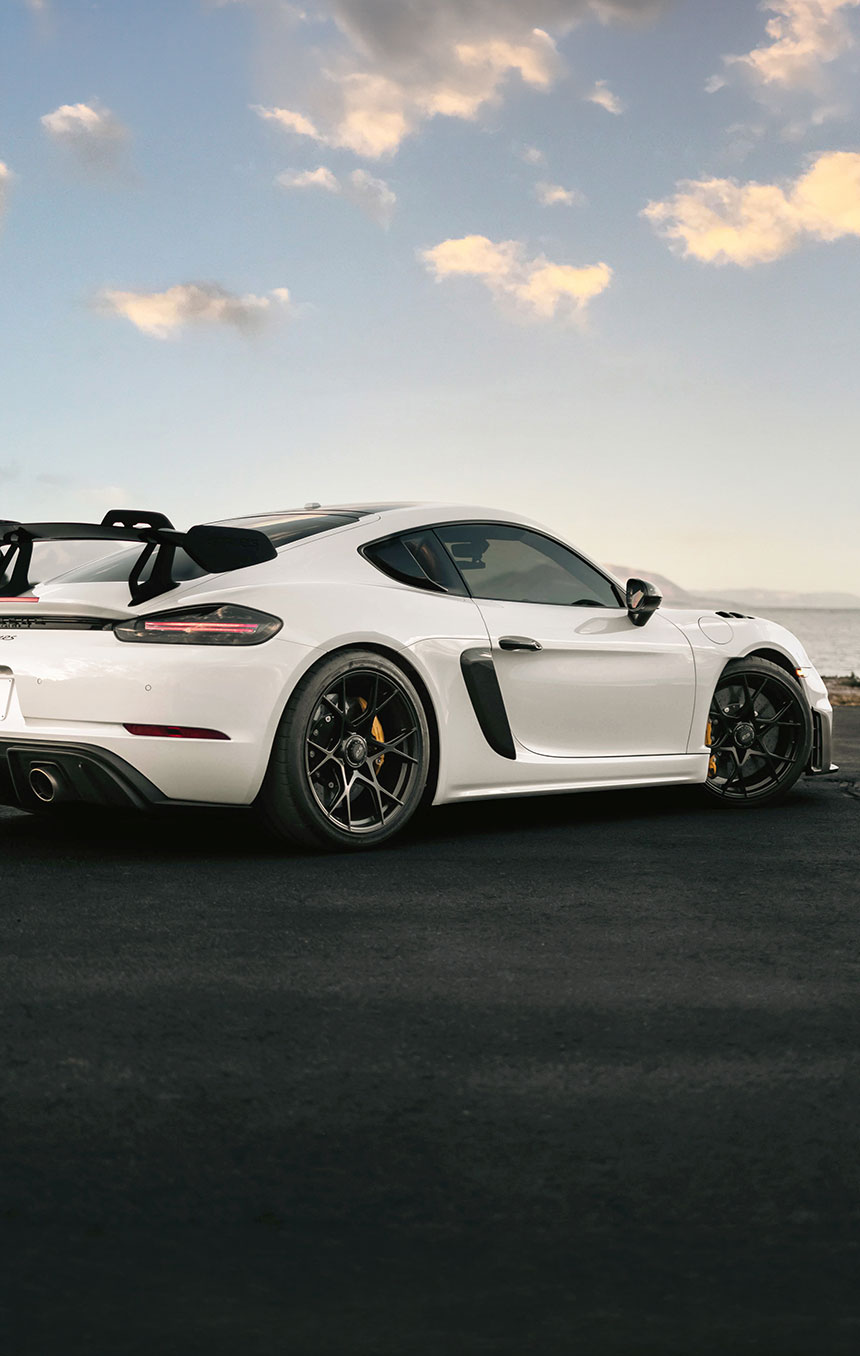 White sports car parked on an open waterfront road at sunset, showcasing a clean exterior finish ideal for enhancing and protecting with automotive paint protection film. 