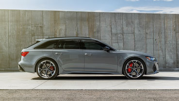 A gray performance wagon parked beside a tall concrete wall, shown from a side profile under bright daylight.