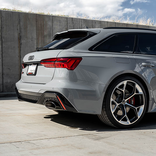 A gray performance wagon photographed from the rear three‑quarter angle, parked on a concrete surface beside a tall concrete wall.