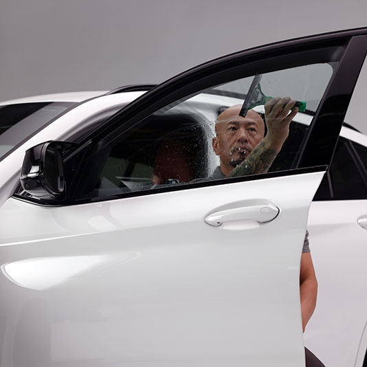 Installer applying window tint to the front door glass of a white vehicle in a professional shop setting.