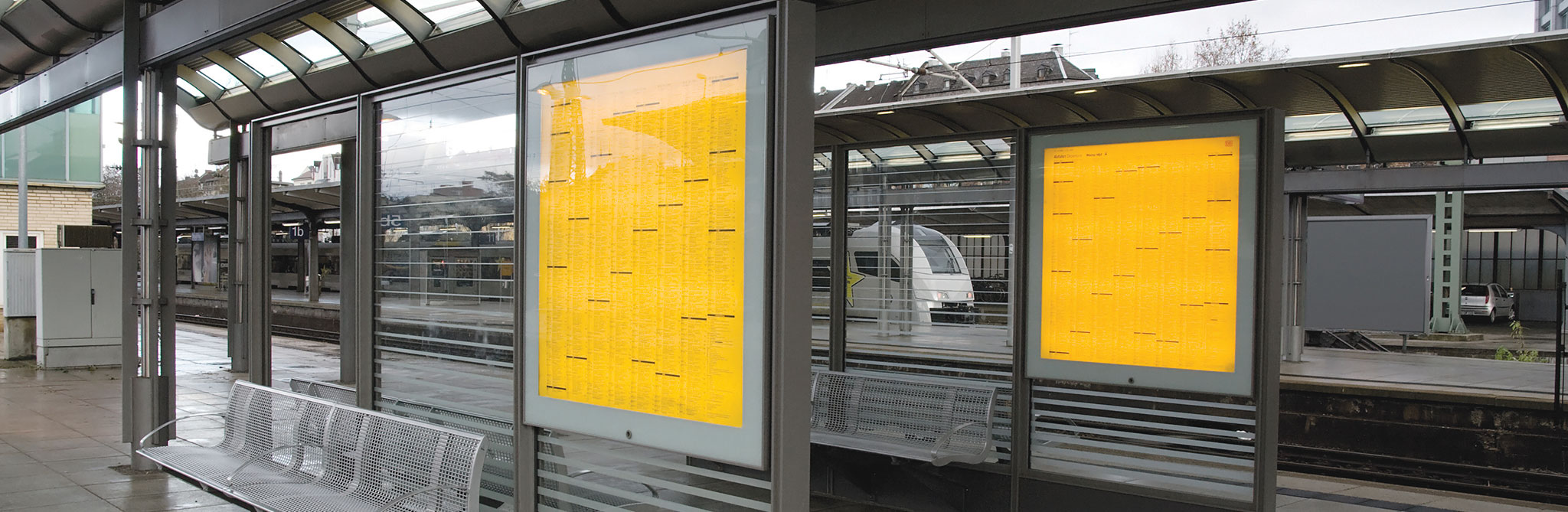 Train station platform with large glass schedule boards and seating. 