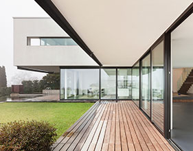 Modern home exterior with large glass walls and a wooden deck.