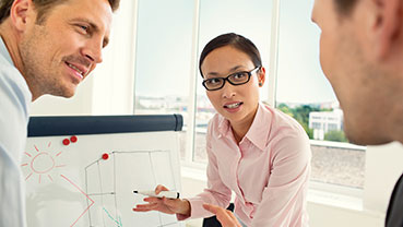 Group discussing drawings on a whiteboard in a brightly lit office.