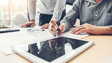 People reviewing architectural plans and using a tablet at a desk.