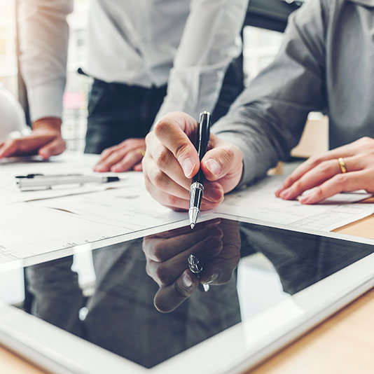 People reviewing architectural plans and using a tablet at a desk.