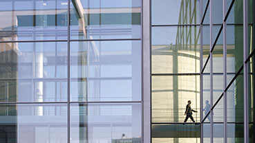 Glass‑walled building interior with a person walking across a skybridge.