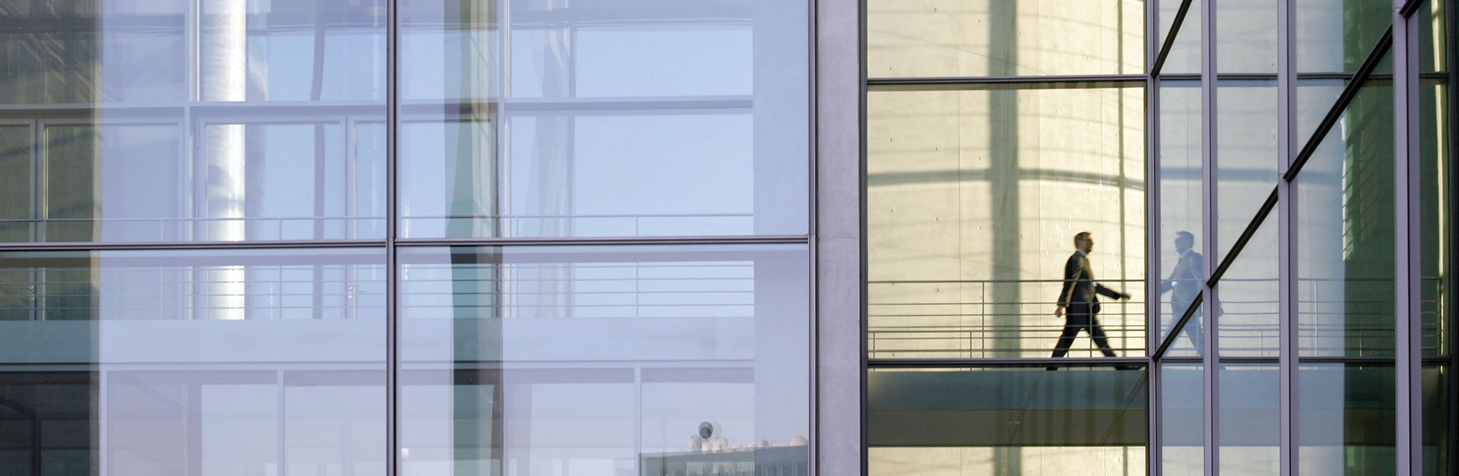Glass‑walled building interior with a person walking across a skybridge. 