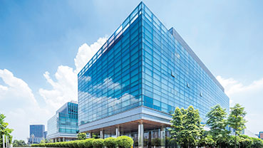 Glass‑clad office complex with trees and shrubs along the walkway.