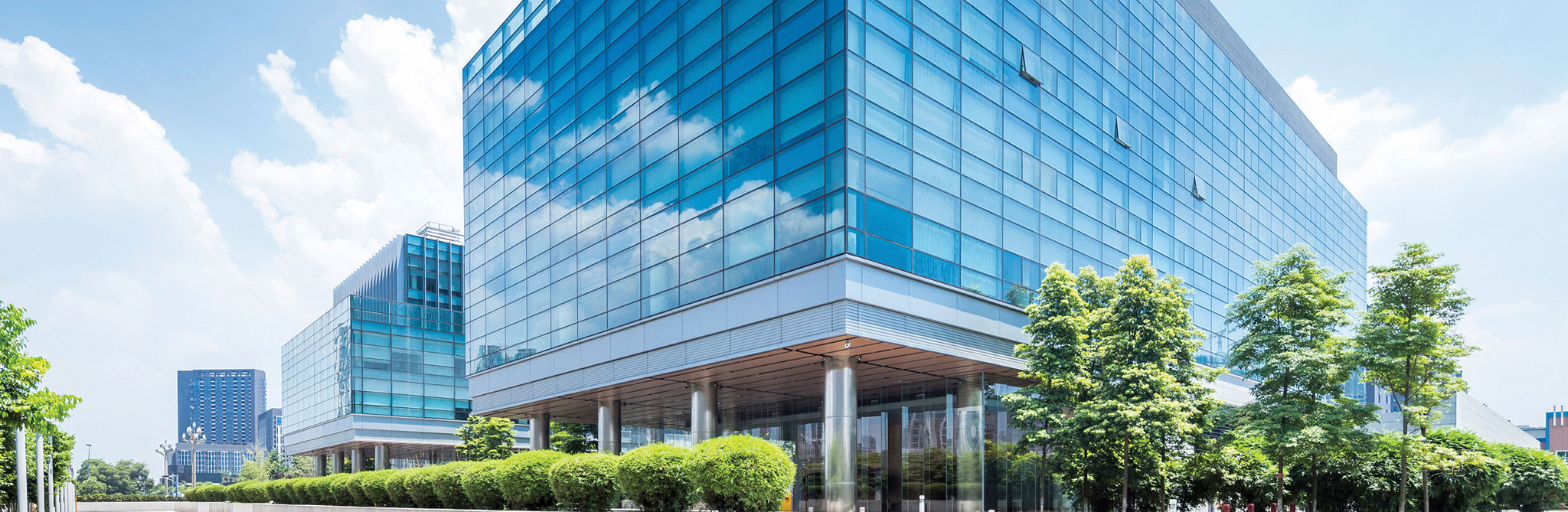 Glass‑clad office complex with trees and shrubs along the walkway. 