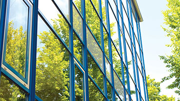 Exterior glass building facade reflecting green trees.