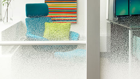 Blue lounge chair with a bright green pillow, partially obscured by textured frosted glass, with a colorful striped artwork on the wall behind it.