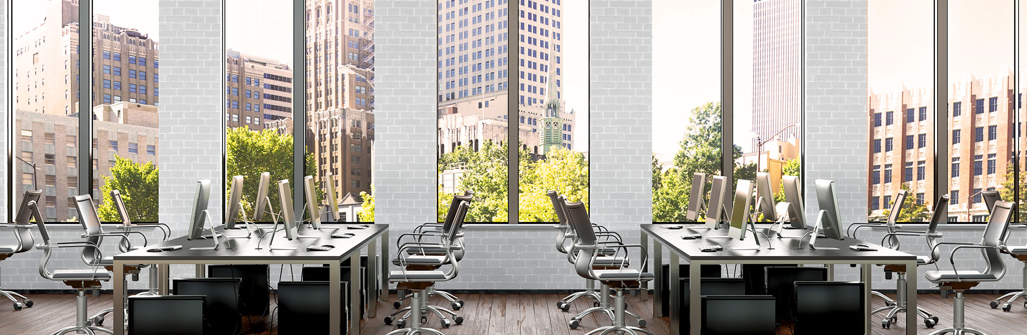 Open office lined with desks and computers overlooking a city skyline. 