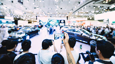 Crowd photographing cars on display at an indoor auto show.
