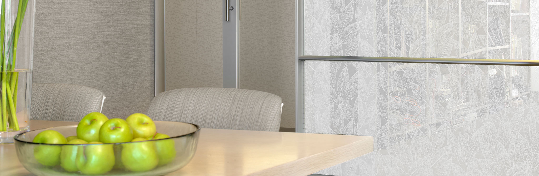 Light-colored meeting area with a bowl of green apples on the table, next to a glass partition featuring a white leaf-patterned privacy film. 