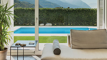 Indoor seating area facing a backyard pool and hedge.