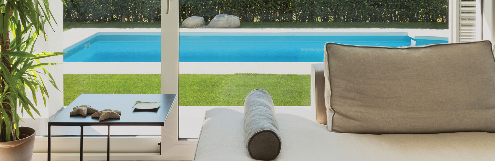 Indoor seating area facing a backyard pool and hedge. 