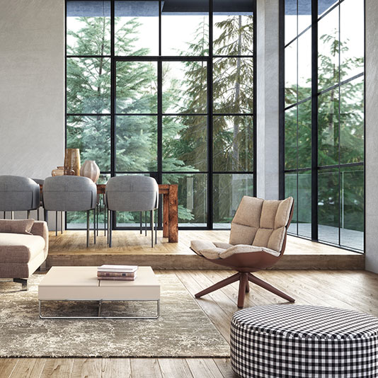Modern living room with floor‑to‑ceiling windows, featuring a lounge chair, low coffee table, textured rug, and a dining area overlooking tall trees.