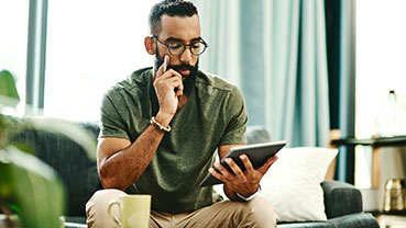 Person sitting on a couch using a tablet with a mug on the table.