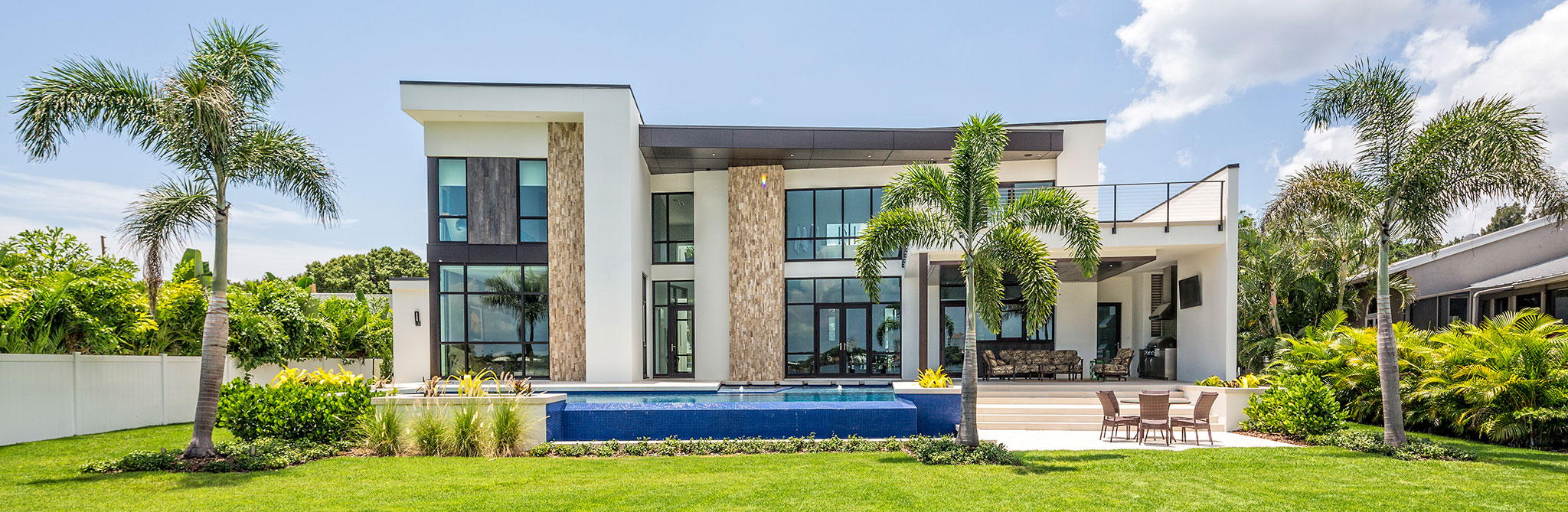 Modern two‑story home with large glass windows, a pool, palm trees, and a landscaped backyard. 