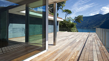 Wooden deck beside a modern glass-walled home with lake views.