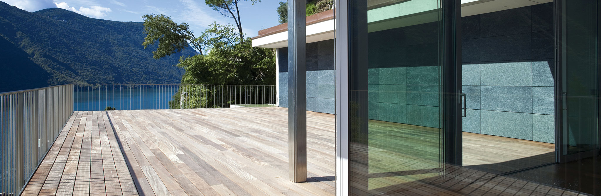 Wooden deck beside a modern glass-walled home with lake views. 