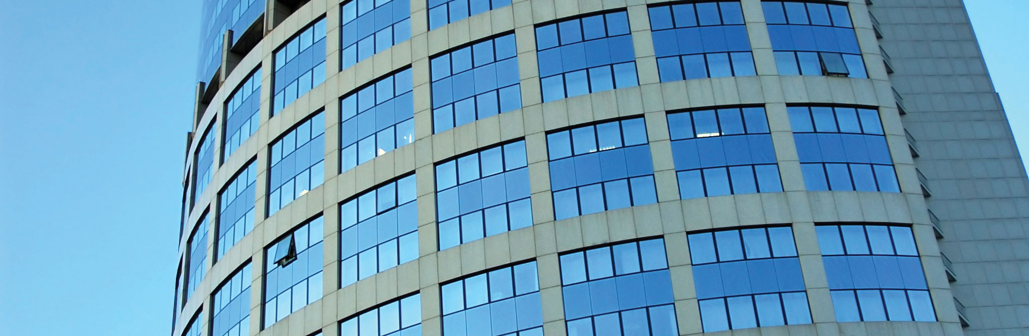 Curved high‑rise building with rows of blue windows against the sky. 
