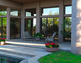 Patio seating area outside a home with large windows and garden views.