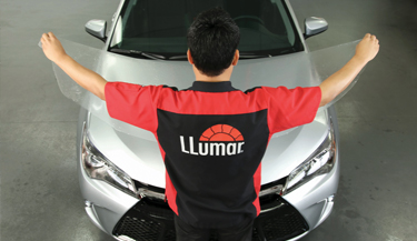 Instaladores LLumar colocando la película de protección de pintura (PPF) en el capó de un auto plateado. 